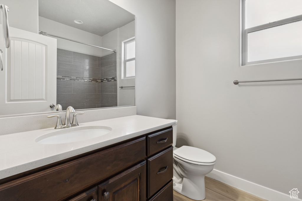 Bathroom featuring toilet, vanity, wood finished floors, baseboards, and a shower