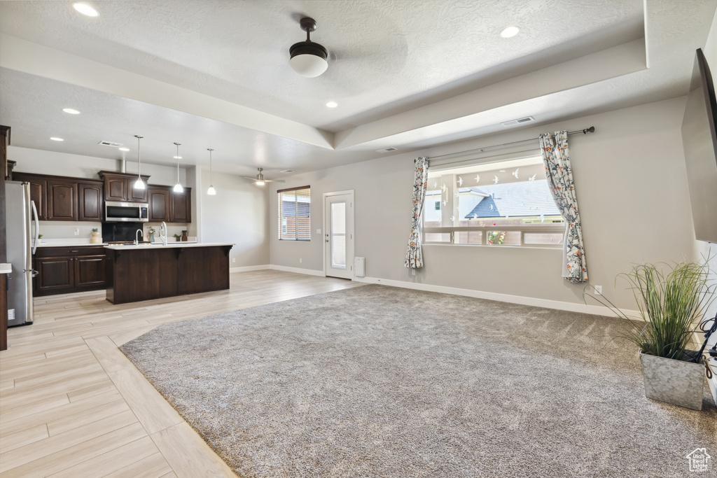 Unfurnished living room featuring a ceiling fan, baseboards, a raised ceiling, recessed lighting, and a textured ceiling