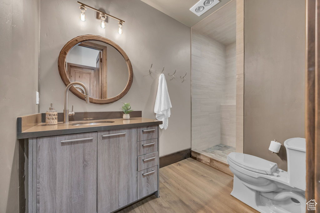 Full bathroom featuring toilet, wood finished floors, vanity, and a tile shower