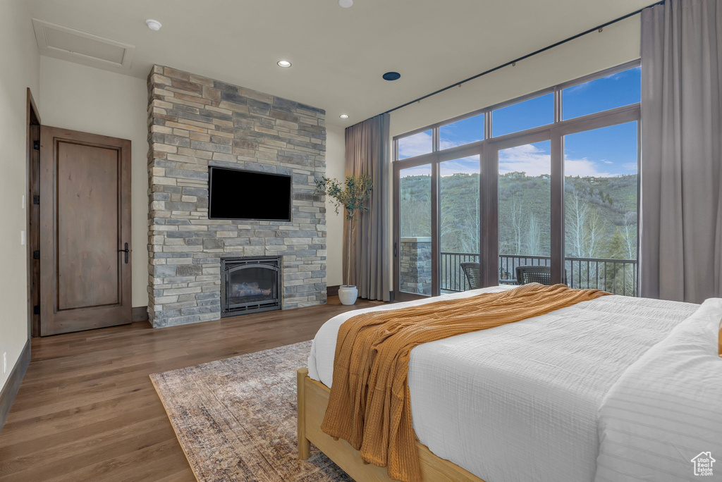 Bedroom with wood finished floors, recessed lighting, a stone fireplace, access to outside, and attic access
