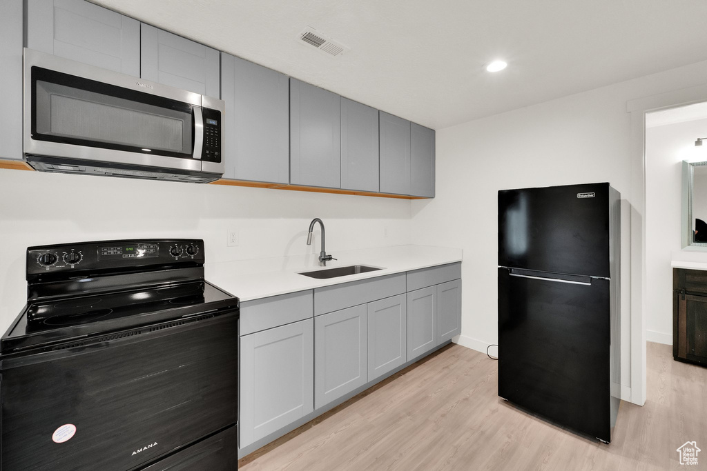Kitchen with black appliances, light wood-type flooring, a sink, gray cabinetry, and recessed lighting
