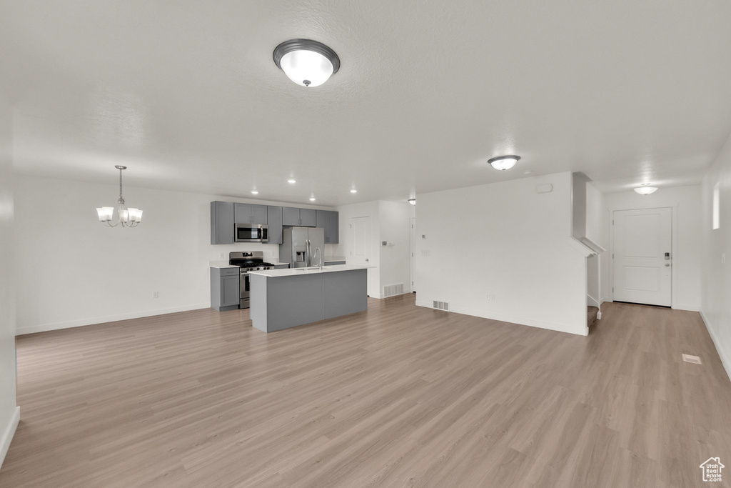 Unfurnished living room featuring a chandelier, baseboards, light wood-style floors, stairway, and recessed lighting
