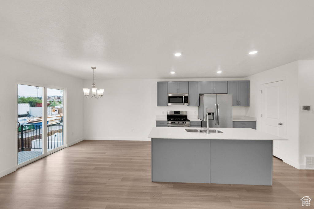 Kitchen with stainless steel appliances, gray cabinetry, a sink, a chandelier, and light countertops