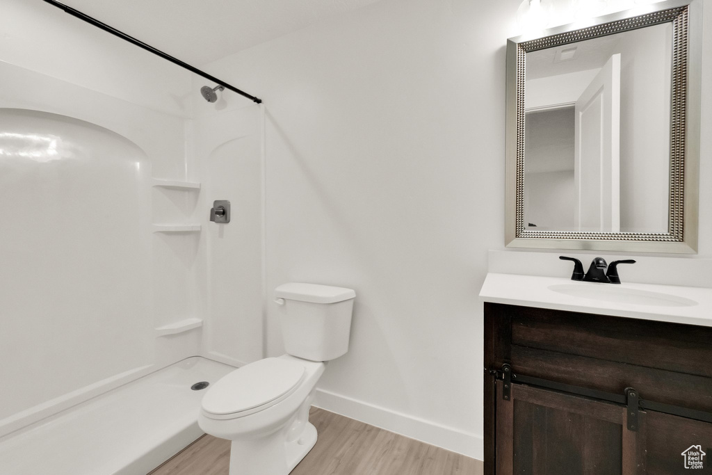Full bath with wood finished floors, vanity, toilet, a shower, and baseboards