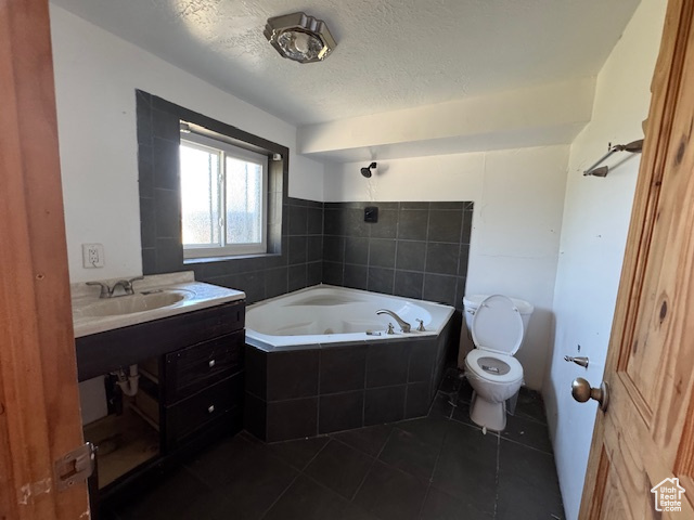 Full bathroom with tile patterned floors, toilet, a relaxing tiled tub, a textured ceiling, and vanity
