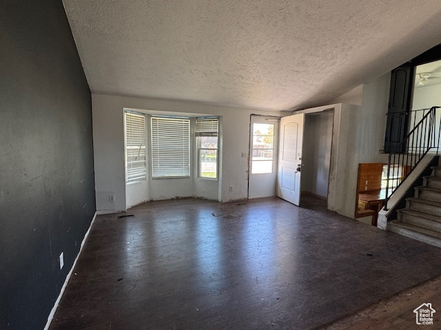 Unfurnished living room with a textured ceiling, stairs, wood finished floors, and baseboards