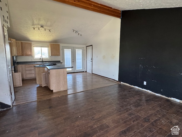 Kitchen featuring light brown cabinetry, dark countertops, a sink, dark wood-style flooring, and a center island
