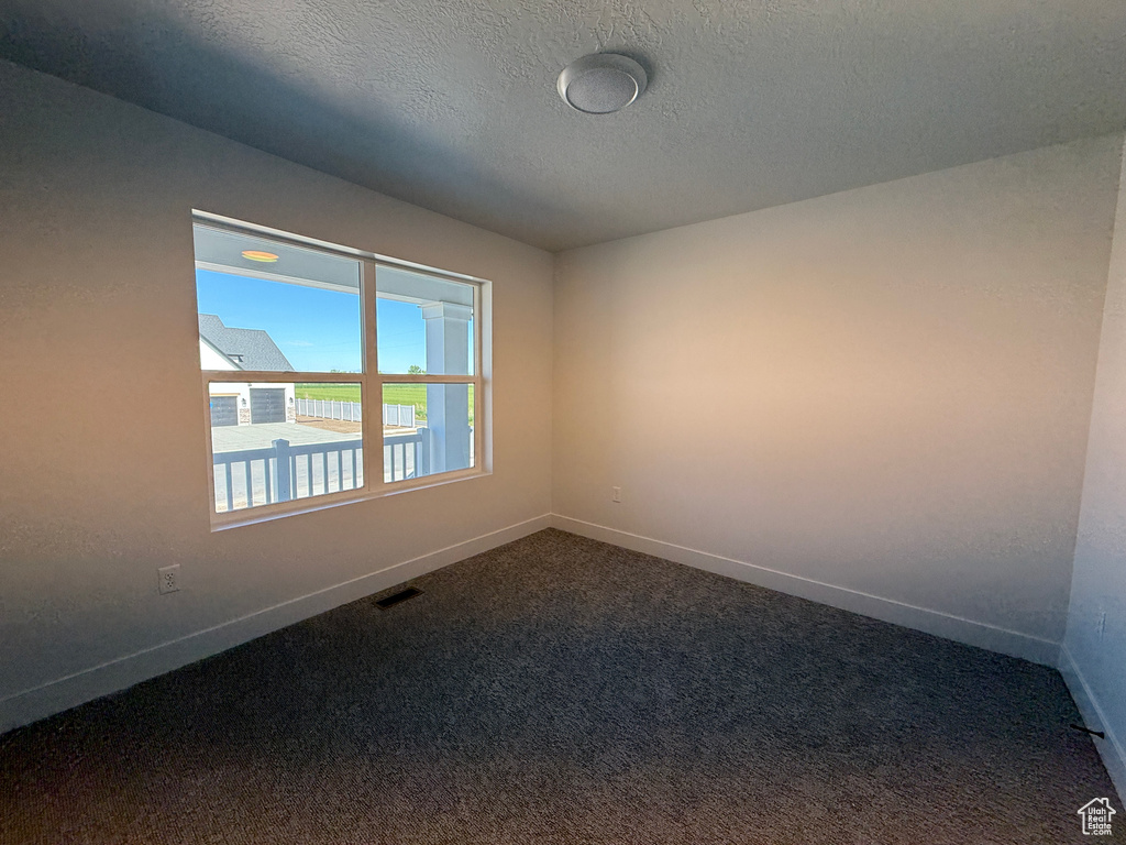 Unfurnished room featuring baseboards, dark colored carpet, and a textured ceiling