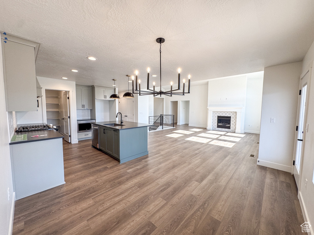 Kitchen featuring dark countertops, wood finished floors, appliances with stainless steel finishes, a kitchen island with sink, and a textured ceiling