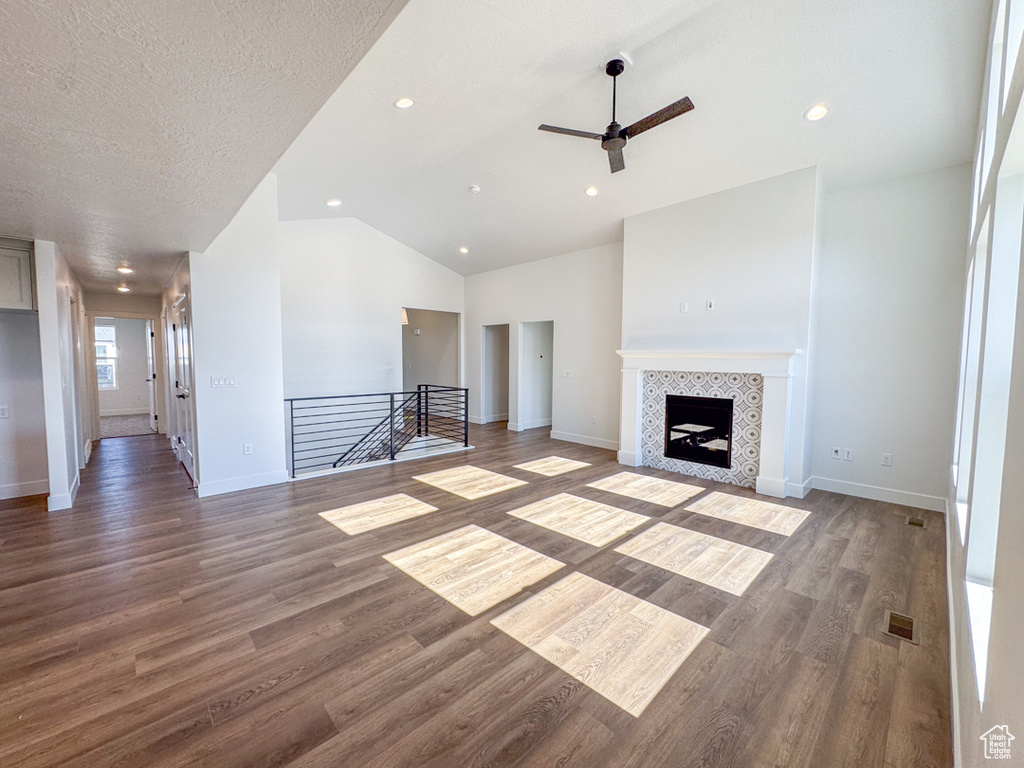 Unfurnished living room featuring ceiling fan, lofted ceiling, wood finished floors, a tiled fireplace, and recessed lighting