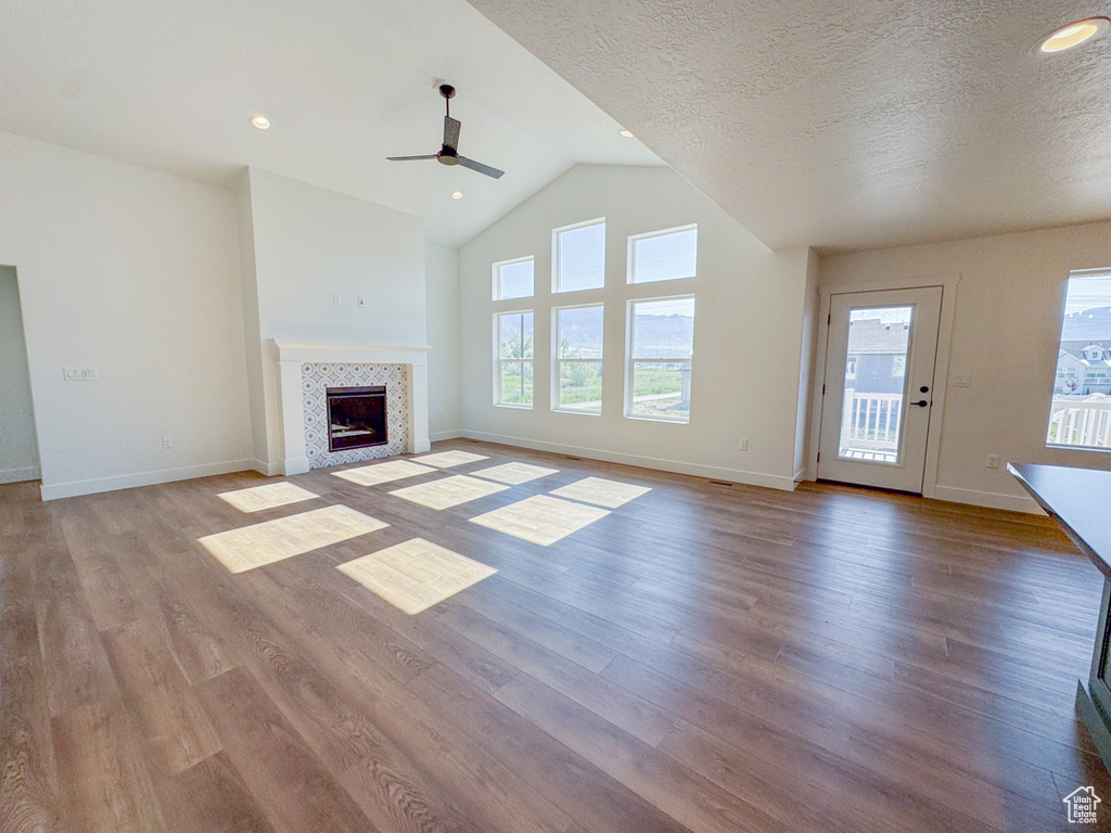 Unfurnished living room with a ceiling fan, wood finished floors, a fireplace, vaulted ceiling, and a textured ceiling