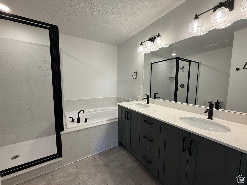 Bathroom featuring a shower stall, a textured ceiling, double vanity, and a bath