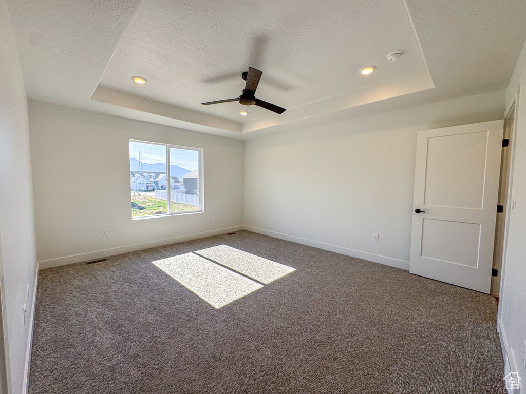 Empty room with a raised ceiling, ceiling fan, carpet floors, a smoke detector, and a textured ceiling