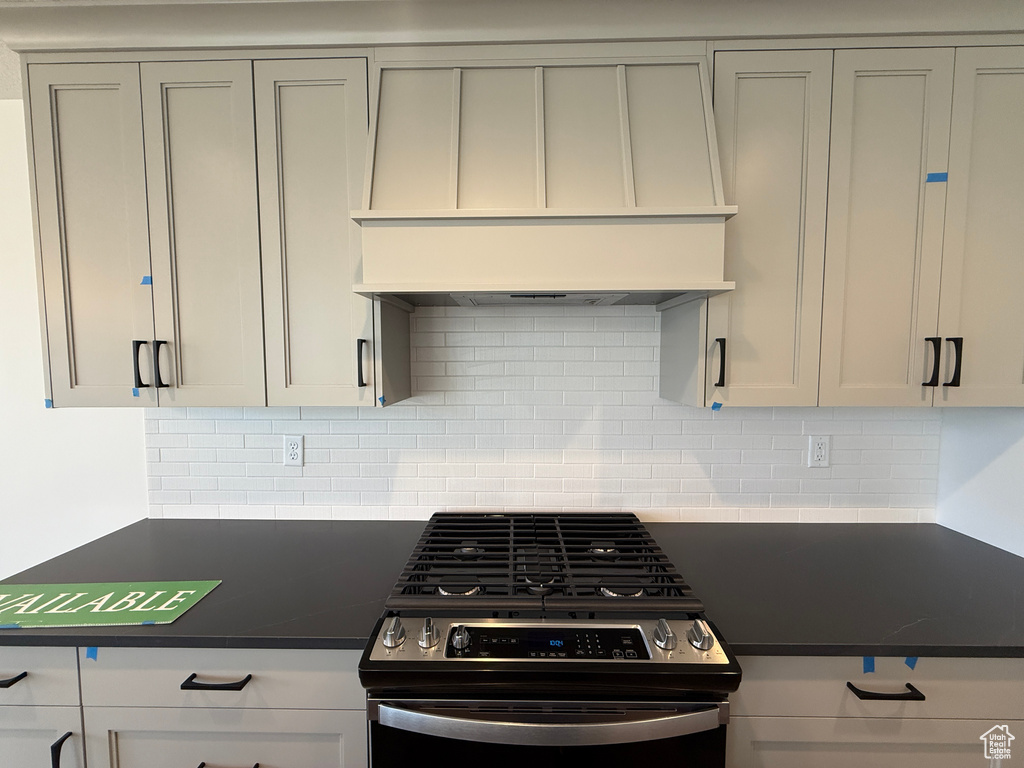 Kitchen featuring stainless steel gas range oven, dark countertops, custom range hood, and tasteful backsplash