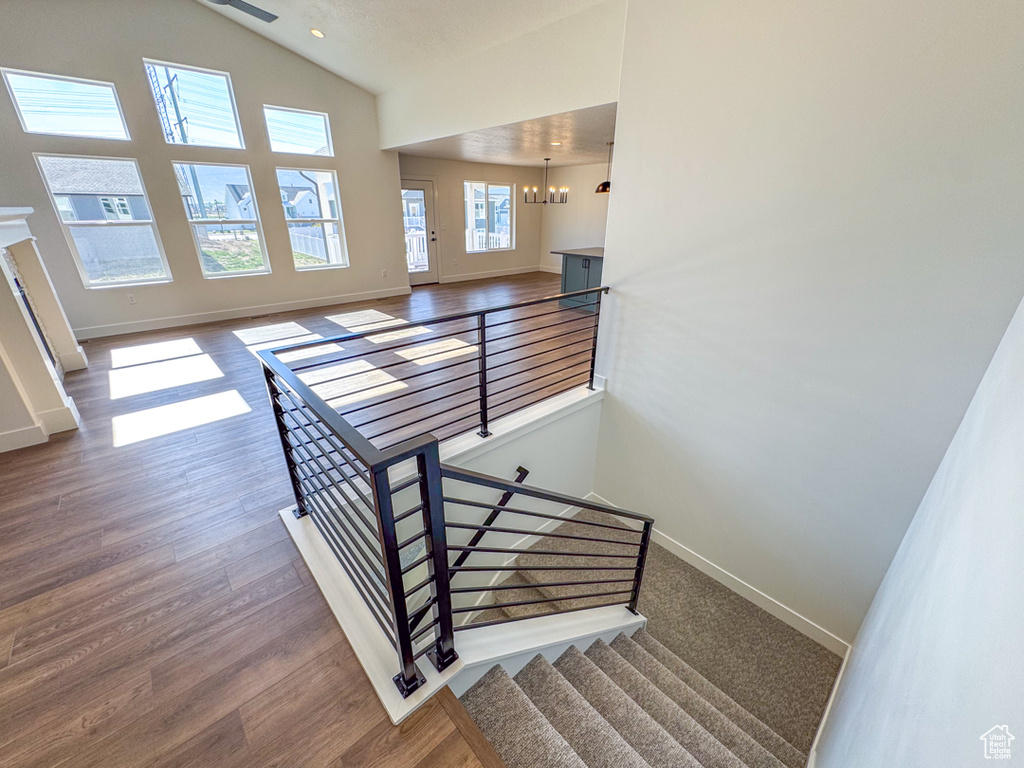 Stairs with a chandelier, wood finished floors, and high vaulted ceiling