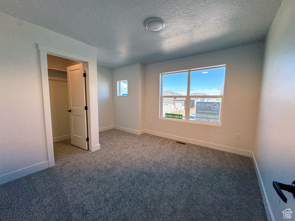 Unfurnished bedroom featuring carpet floors, a textured ceiling, and a walk in closet