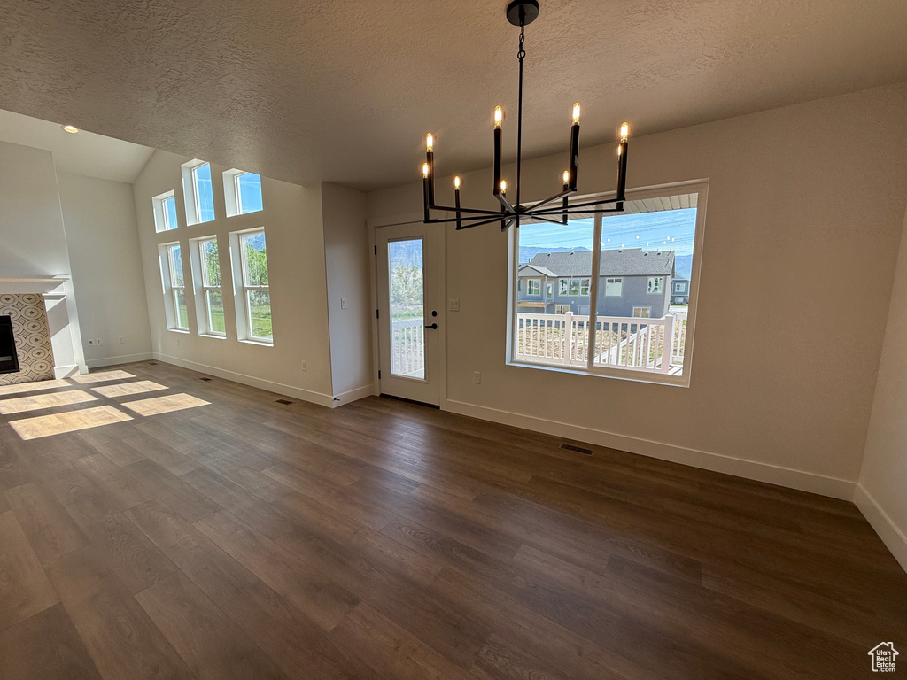 Unfurnished living room with baseboards, dark wood-type flooring, a chandelier, a textured ceiling, and a tile fireplace