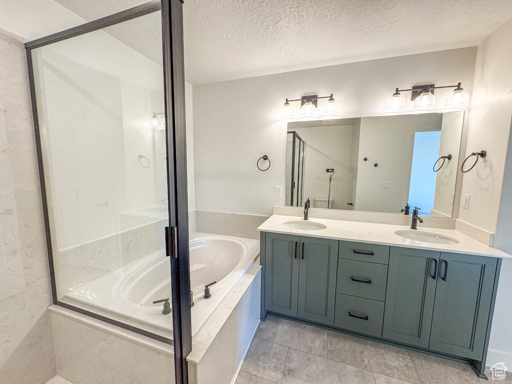 Full bathroom featuring a garden tub, double vanity, an enclosed shower, and a textured ceiling
