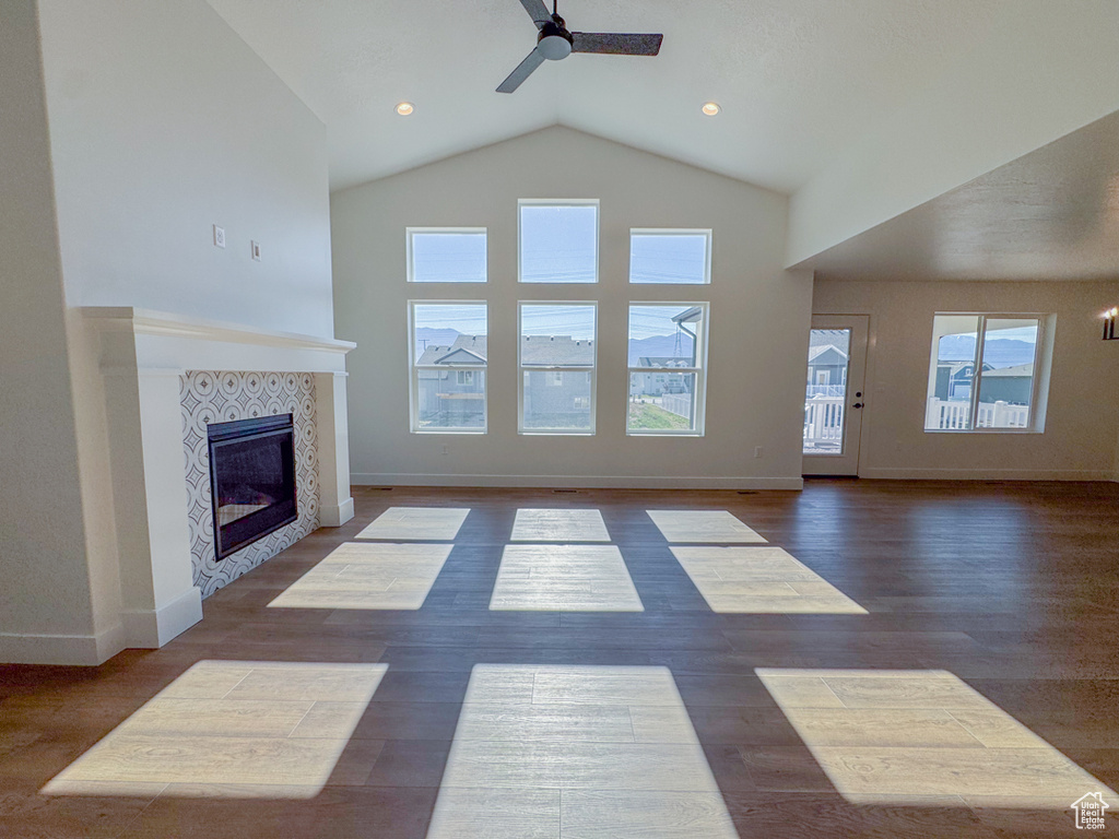 Unfurnished living room featuring ceiling fan, a tile fireplace, high vaulted ceiling, and dark wood-style flooring