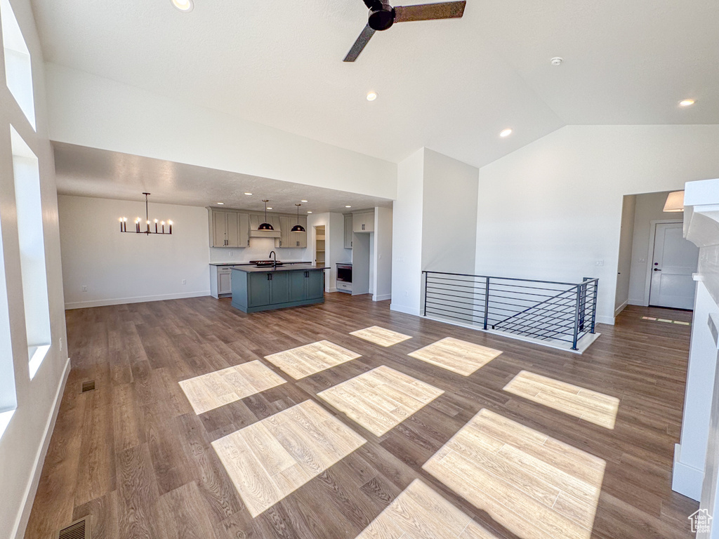 Unfurnished living room featuring ceiling fan, a chandelier, lofted ceiling, wood finished floors, and recessed lighting