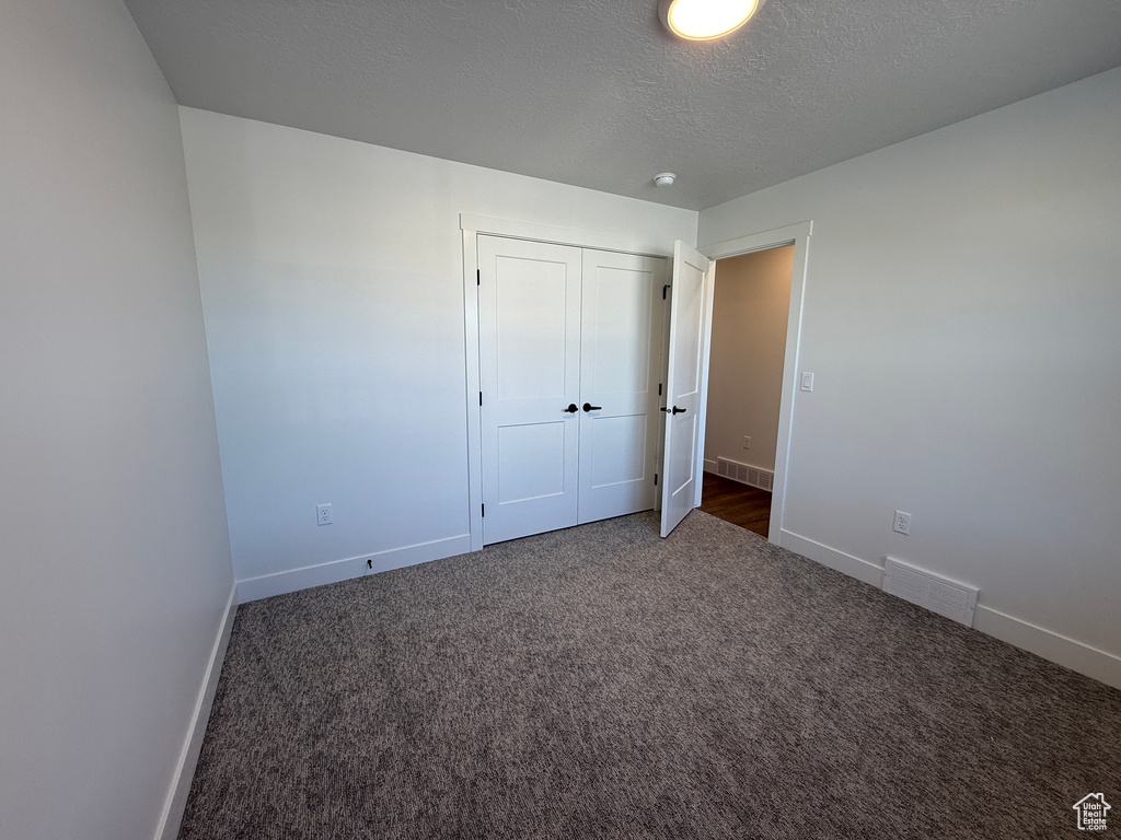 Unfurnished bedroom with baseboards, carpet, a textured ceiling, and a closet