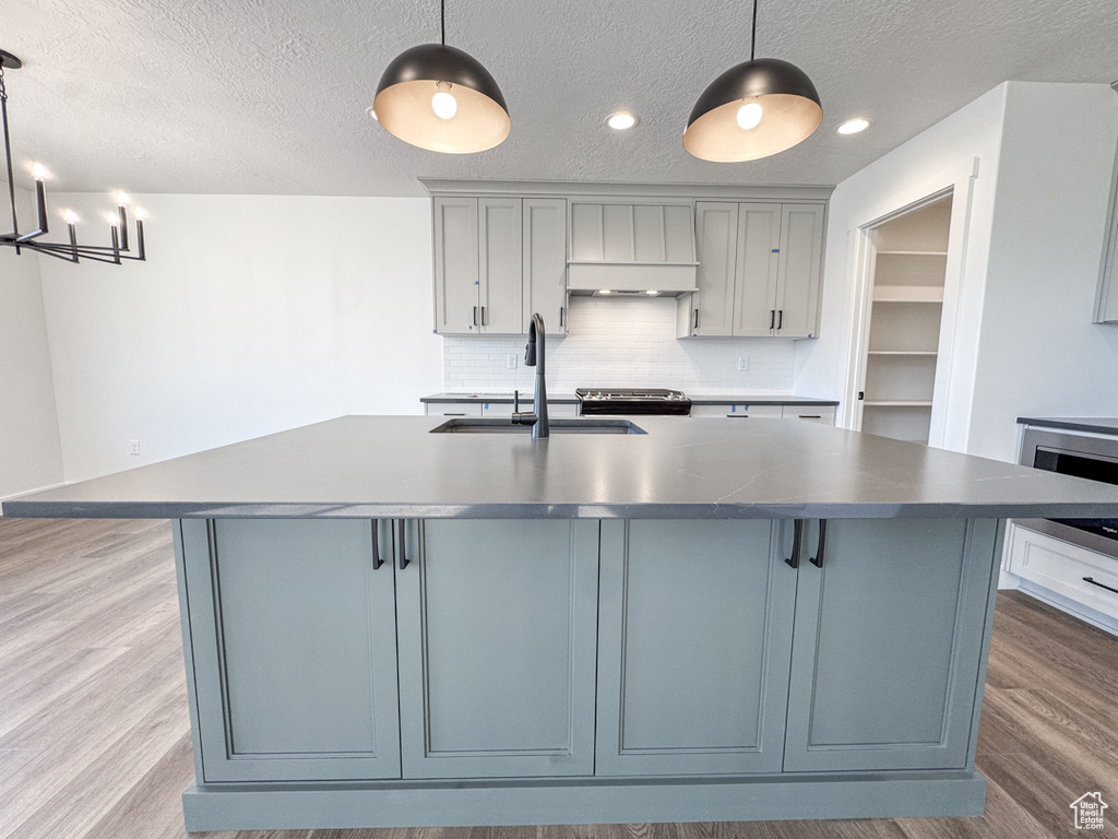 Kitchen featuring exhaust hood, gray cabinets, wood finished floors, a textured ceiling, and recessed lighting