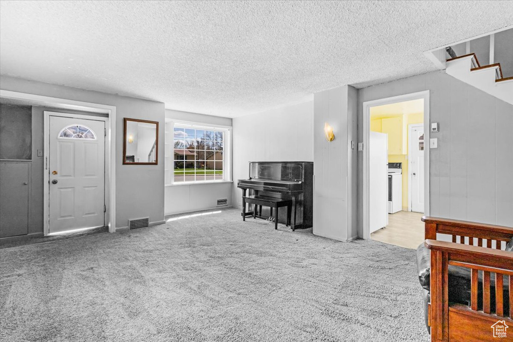 Carpeted living room with a textured ceiling, baseboards, and stairs