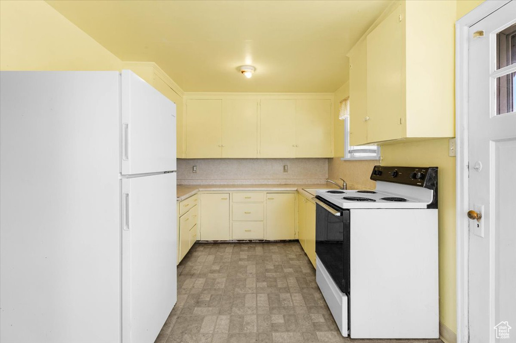 Kitchen with electric range, freestanding refrigerator, light countertops, a sink, and brick patterned flooring