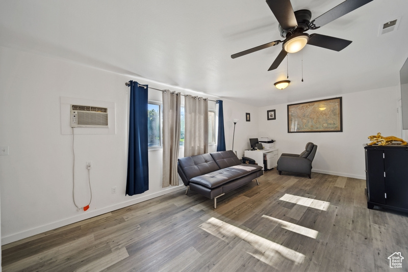 Living room with wood finished floors, a wall mounted air conditioner, a ceiling fan, and baseboards