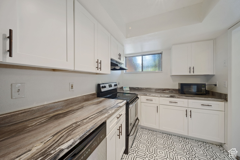 Kitchen featuring stainless steel range with electric cooktop, under cabinet range hood, black microwave, and white cabinetry