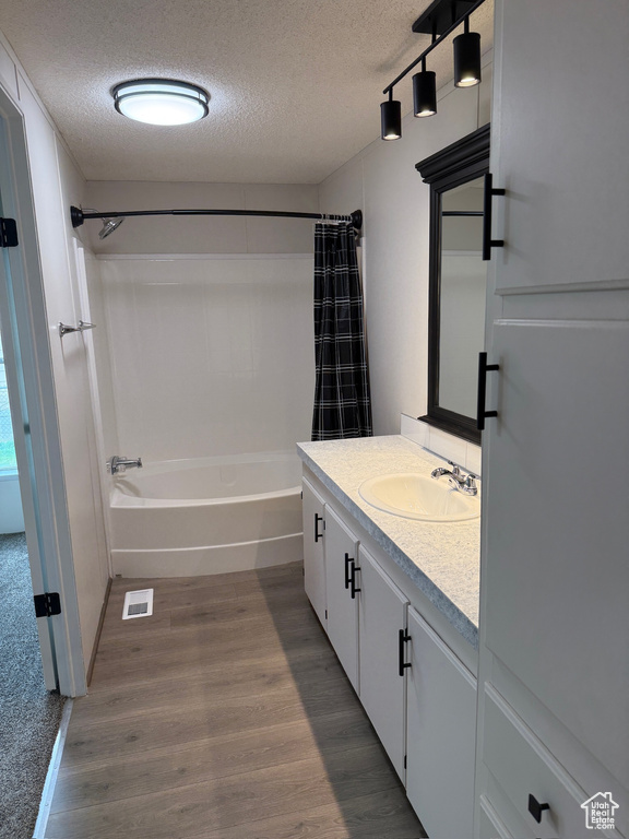 Bathroom with a textured ceiling, wood finished floors, shower / bath combo, and vanity
