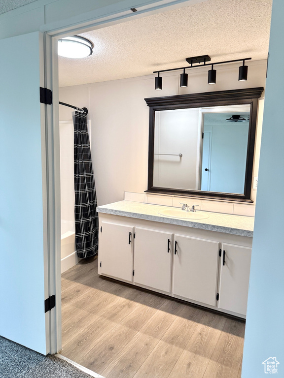 Bathroom with wood finished floors, vanity, a textured ceiling, and shower / tub combo with curtain