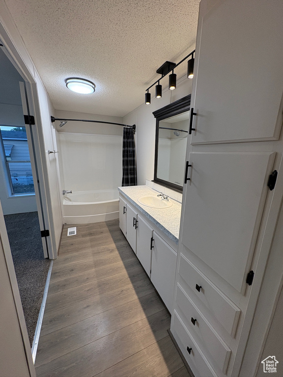 Bathroom featuring a textured ceiling, vanity, shower / tub combo with curtain, wood finished floors, and track lighting