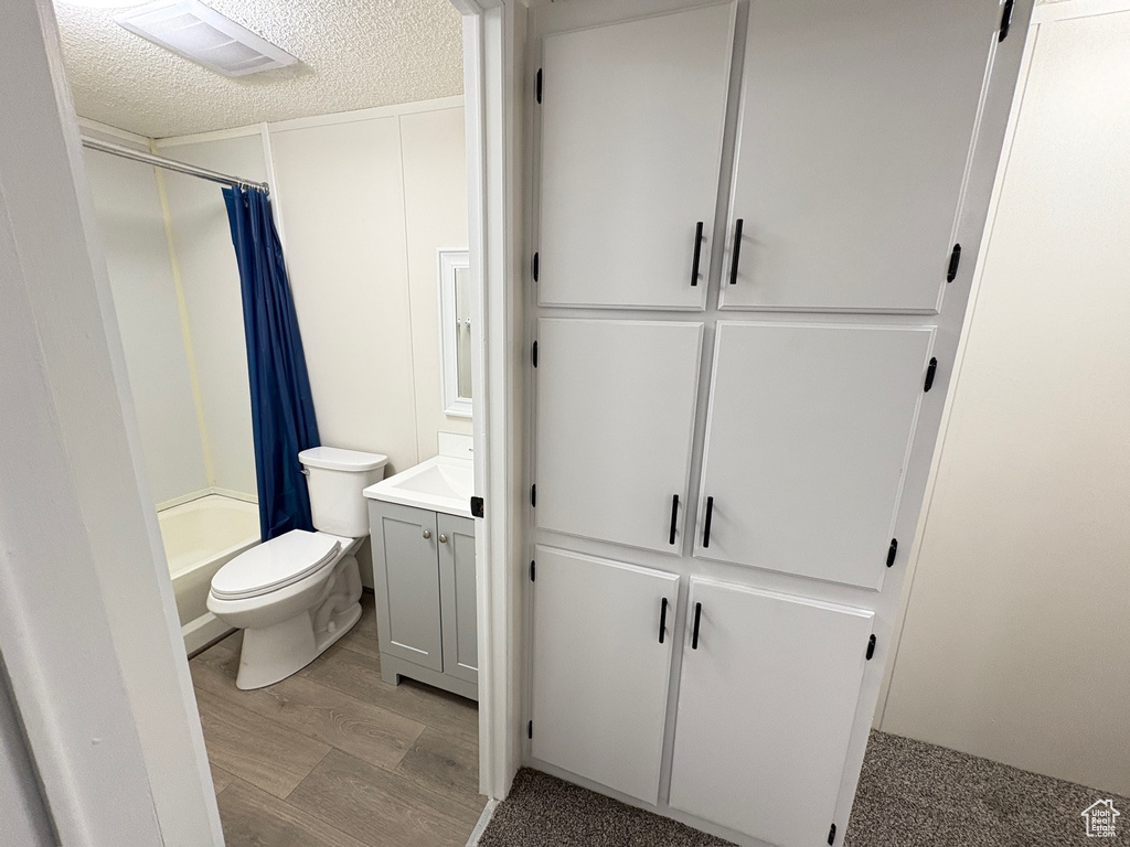 Full bath featuring wood finished floors, vanity, a textured ceiling, toilet, and shower / tub combo