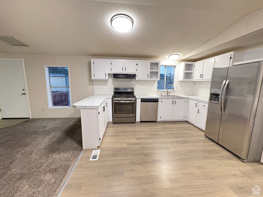 Kitchen featuring appliances with stainless steel finishes, a sink, open shelves, extractor fan, and light wood-type flooring