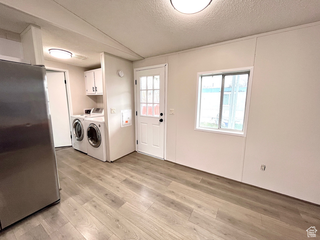 Clothes washing area featuring cabinet space, washer and clothes dryer, light wood-type flooring, and a textured ceiling