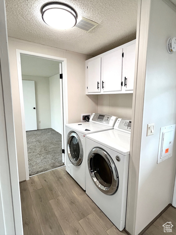 Clothes washing area with washing machine and dryer, cabinet space, light wood-style floors, and a textured ceiling