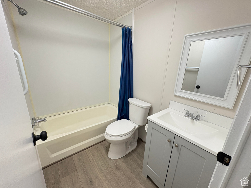 Bathroom featuring wood finished floors, a textured ceiling, shower / tub combo, toilet, and vanity