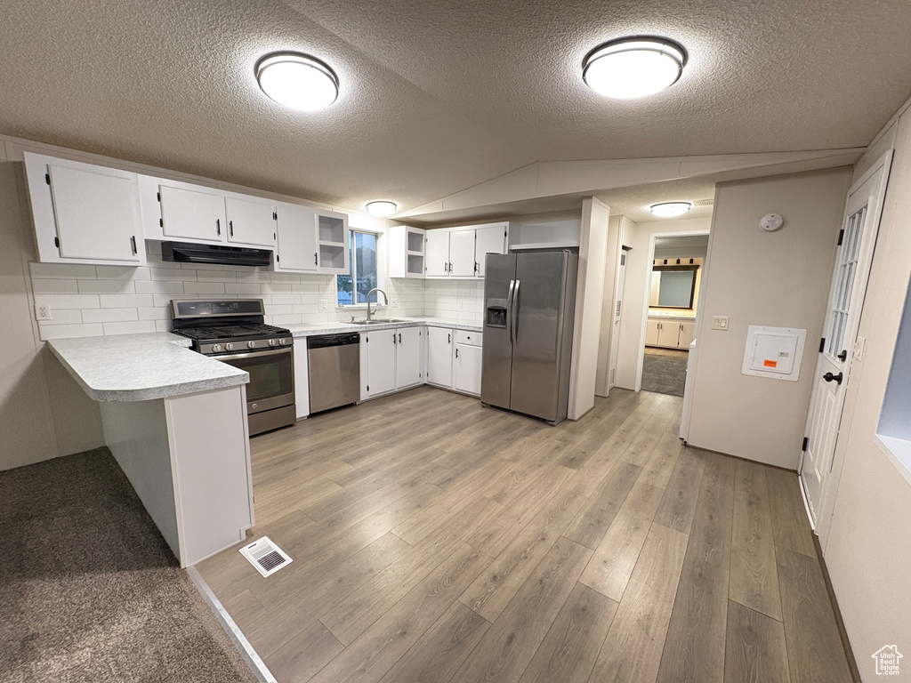 Kitchen with appliances with stainless steel finishes, open shelves, light countertops, light wood-style floors, and under cabinet range hood
