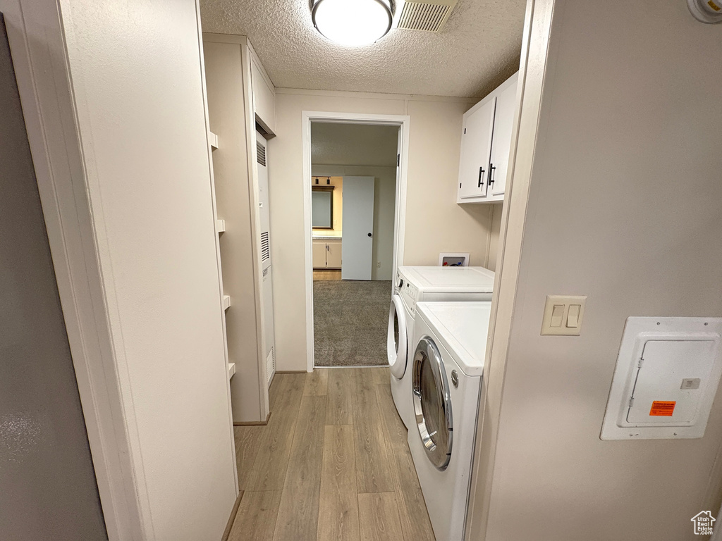 Laundry room with cabinet space, light wood-style floors, washing machine and clothes dryer, a textured ceiling, and electric panel