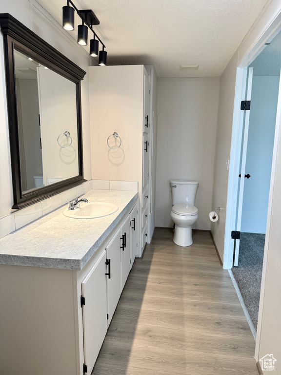 Bathroom with a textured ceiling, toilet, vanity, and wood finished floors