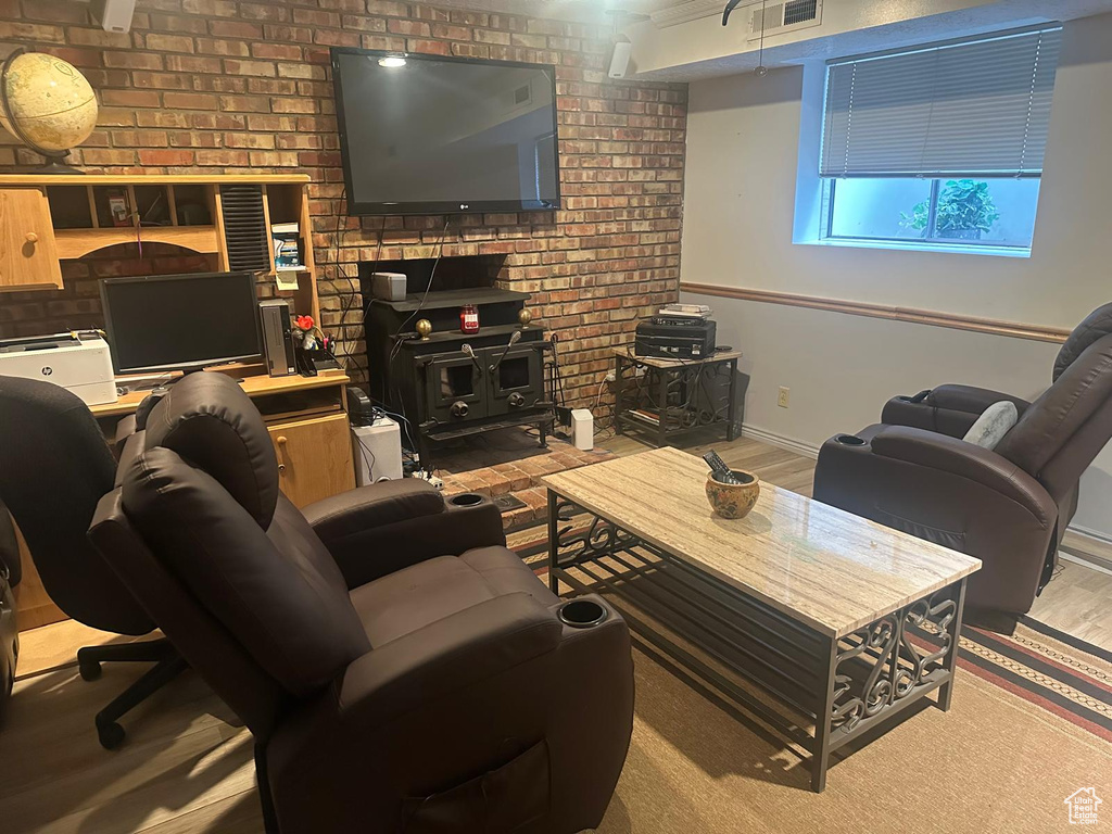 Living room with a wood stove, brick wall, baseboards, wood finished floors, and an office area
