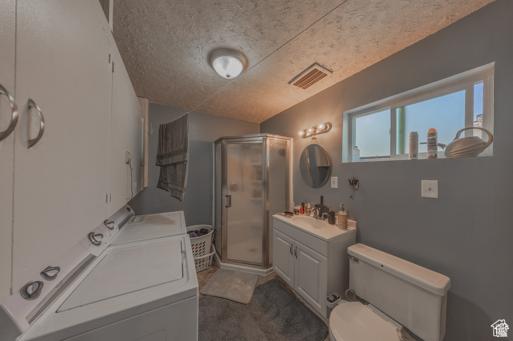 Full bath with washer and clothes dryer, a shower stall, a textured ceiling, toilet, and vanity