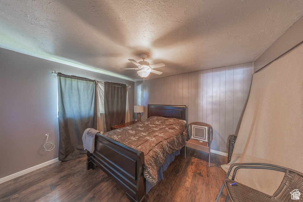 Bedroom with wood finished floors, baseboards, a textured ceiling, a ceiling fan, and wooden walls