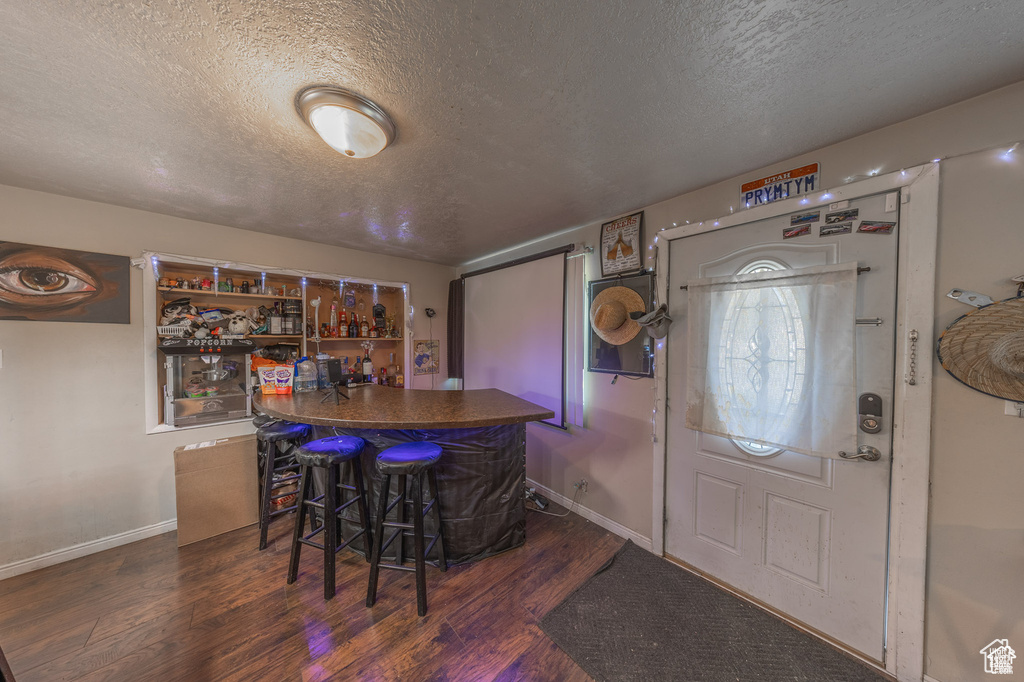 Indoor dry bar with a textured ceiling, wood finished floors, and baseboards