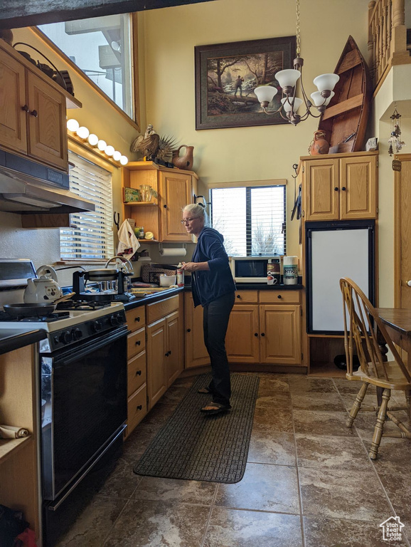 Kitchen with gas range oven, stainless steel microwave, under cabinet range hood, dark countertops, and open shelves