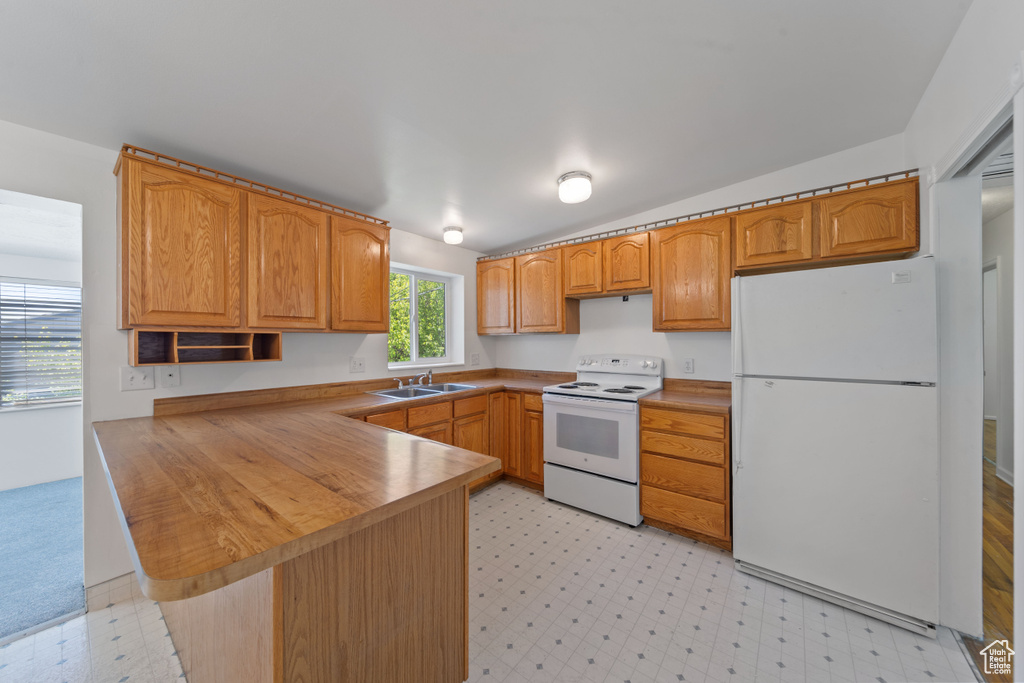 Kitchen featuring white appliances, a sink, light flooring, and a peninsula