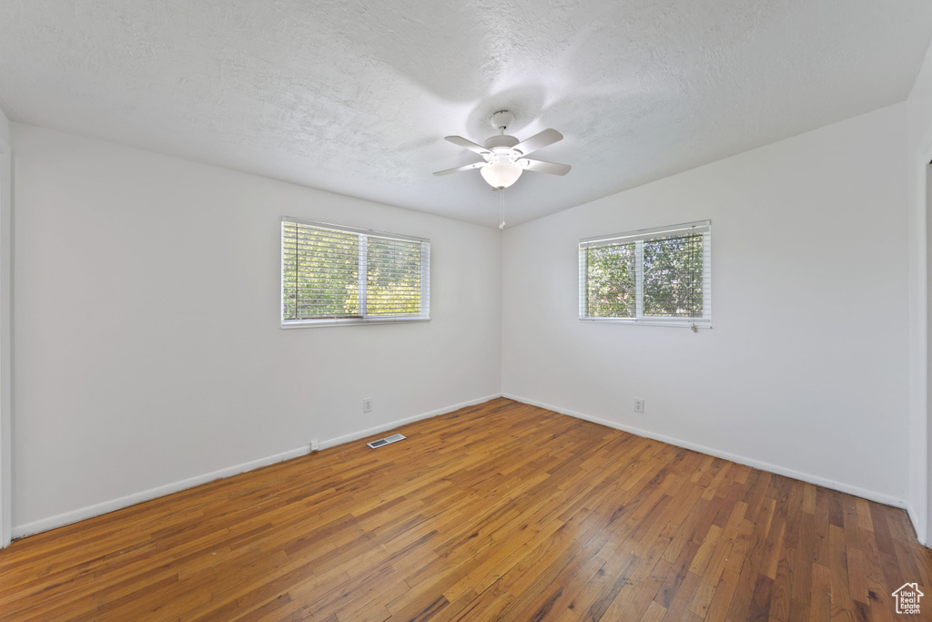 Spare room featuring baseboards, hardwood / wood-style floors, a ceiling fan, and a textured ceiling