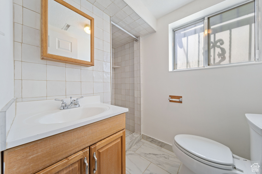 Full bath featuring toilet, tiled shower, marble finish flooring, vanity, and baseboards
