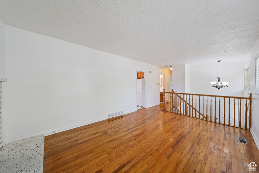 Spare room featuring wood-type flooring, a chandelier, a textured ceiling, and baseboards